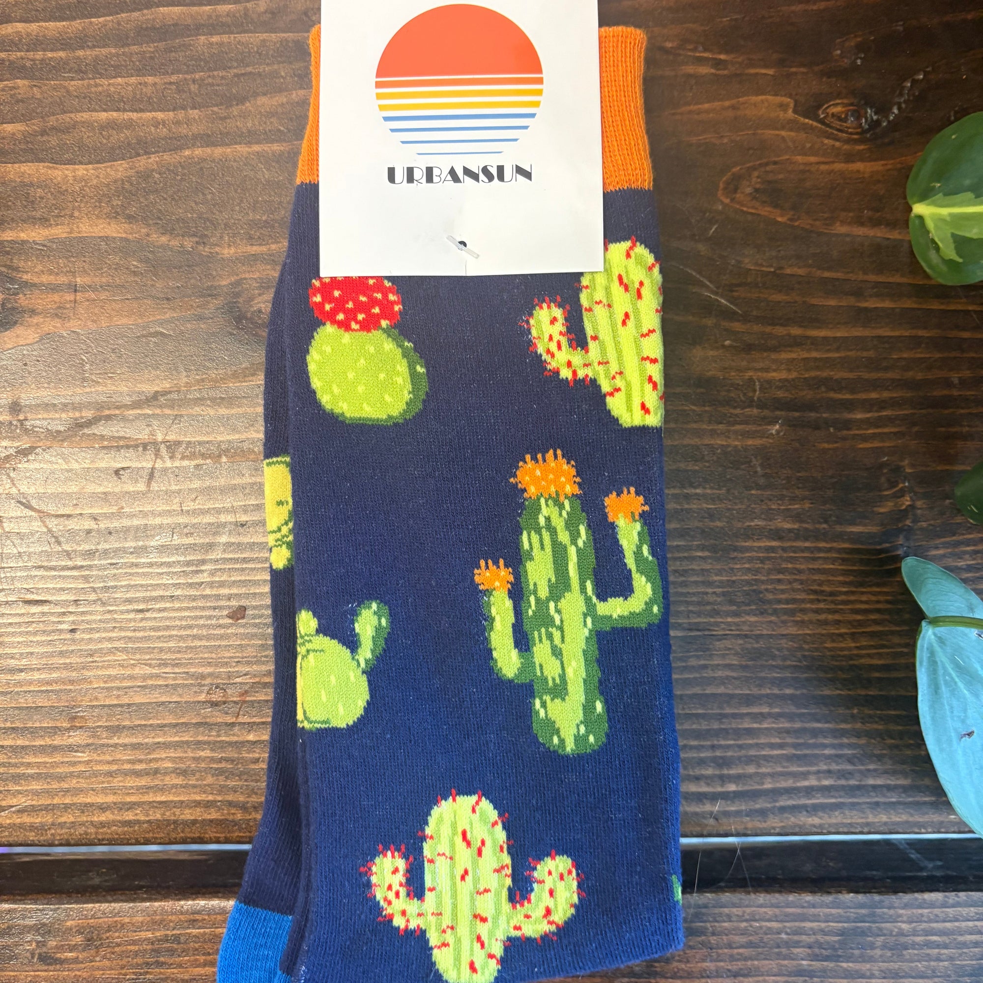 Colorful cactus-patterned socks on a wooden surface with a brand label.
